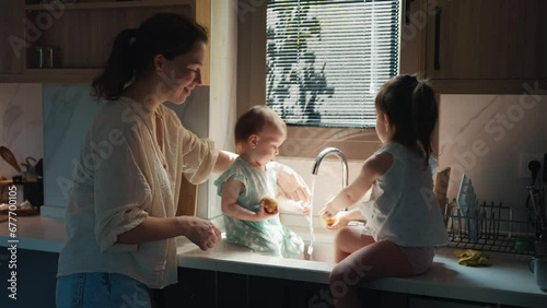 Young Mother and Two Little Baby Girls Playing with Water Flowing from a Tap