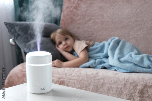 Diffuser White light electric. In the background there is a happy little fair-haired girl, blurred background. The concept of humidifying and aromatizing indoor air.