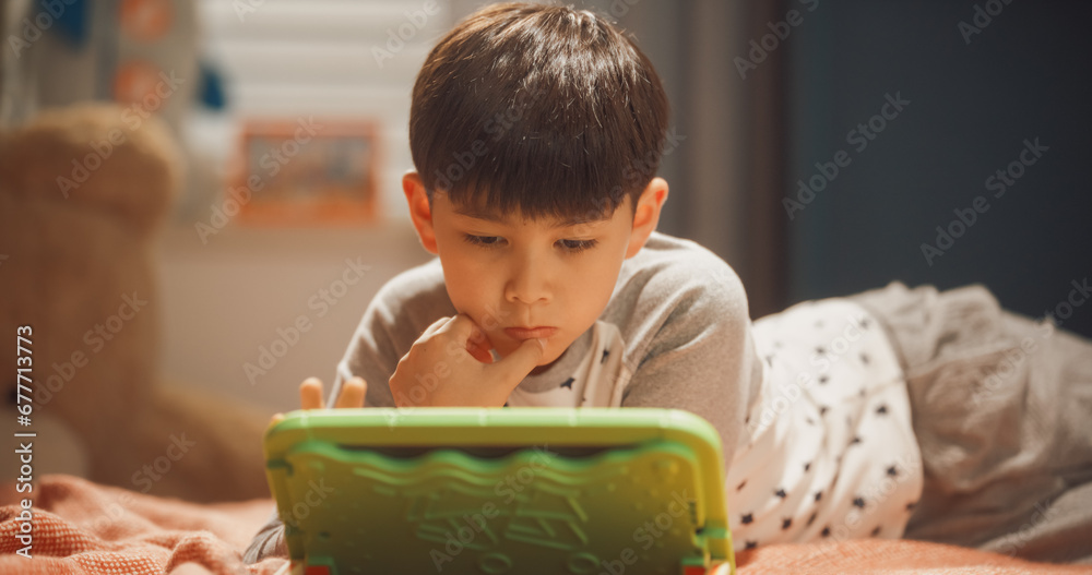 Smart South Korean Boy Playing Educational and Learning Game on a Tablet Computer at Home in His Children's Bedroom. Happy Child Celebrating After Winning Another Round in a Video Game Smart South Korean Boy Playing Educational and Learning Game on a Tablet Computer at Home in His Children's Bedroom. Happy Child Celebrating After Winning Another Round in a Video Game