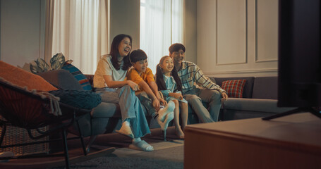 Happy Korean Family At Home: Mother And Father Watching Funny Family Television Show And Laughing With Their Little Son And Daughter On The Couch. Siblings Having Fun With Parents In Living Room.