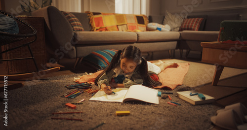 Evening Portrait of Cute Little Girl Drawing while Lying on the Floor in Living Room. Talented Korean Child Being Creative, Coloring Picture, Preparing a Become Famous Artist