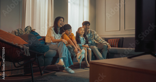 Happy Korean Family At Home: Mother And Father Watching Funny Family Television Show And Laughing With Their Little Son And Daughter On The Couch. Siblings Having Fun With Parents In Living Room.
