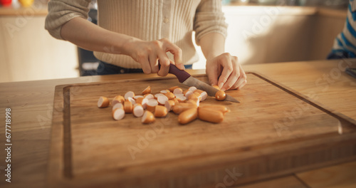Close Up on the Hands of a Beautiful Woman Cutting Sausages in her Kitchen at Home. Focused and Carefree Housewife Using a Knife and a Cutting board to Prepare a Delicious Meal for her Family