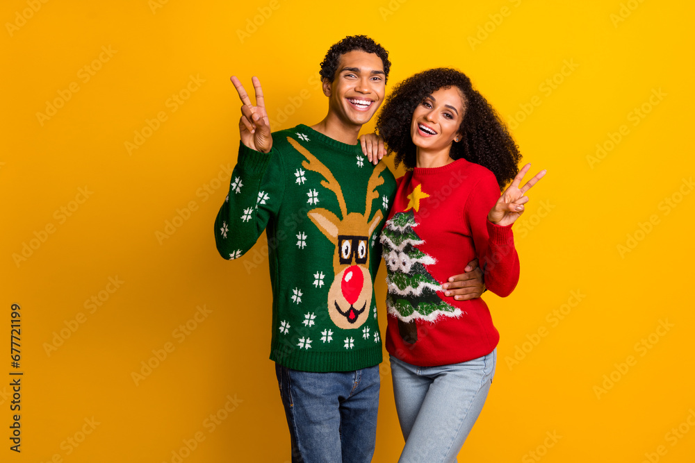 Photo of positive pretty lady guy wear new year ugly print sweaters showing v-signs empty space isolated yellow color background Photo of positive pretty lady guy wear new year ugly print sweaters showing v-signs empty space isolated yellow color background
