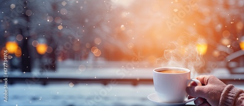  a person holding a cup of coffee with steam rising out of it in front of a snowy cityscape.