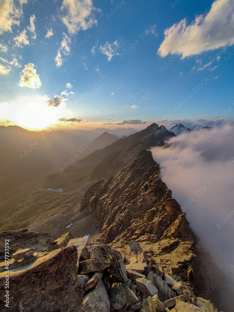 Panoramic view of a mountain range in the Alps on the Italian-French border at sunset. Clouds rising hitting the natural barrier. Piedmont, Italy.