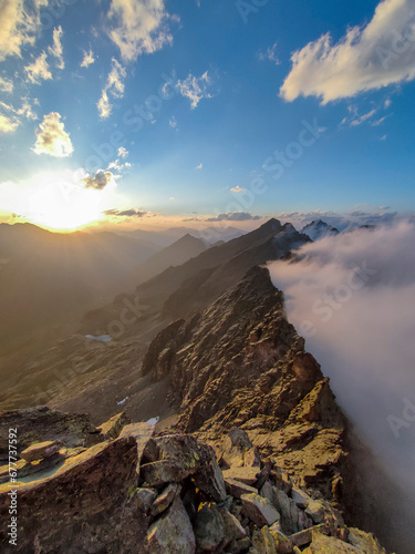 Panoramic view of a mountain range in the Alps on the Italian-French border at sunset. Clouds rising hitting the natural barrier. Piedmont, Italy.