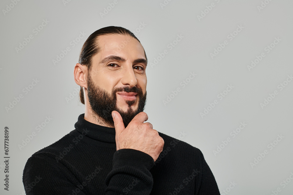 portrait of good looking arabic man in turtleneck touching beard and smiling on grey backdrop portrait of good looking arabic man in turtleneck touching beard and smiling on grey backdrop