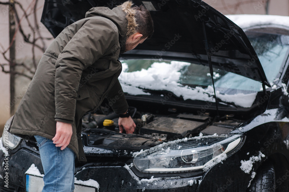 Man open hood of the car and trying to find out what is happened with car. Man scratches the back of is head. Winter outdoors Man open hood of the car and trying to find out what is happened with car. Man scratches the back of is head. Winter outdoors
