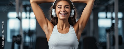 dark skinned woman in good mood, raises arm with muscles, has strong body, dressed in gym outfit, listens audio, Generative AI photo