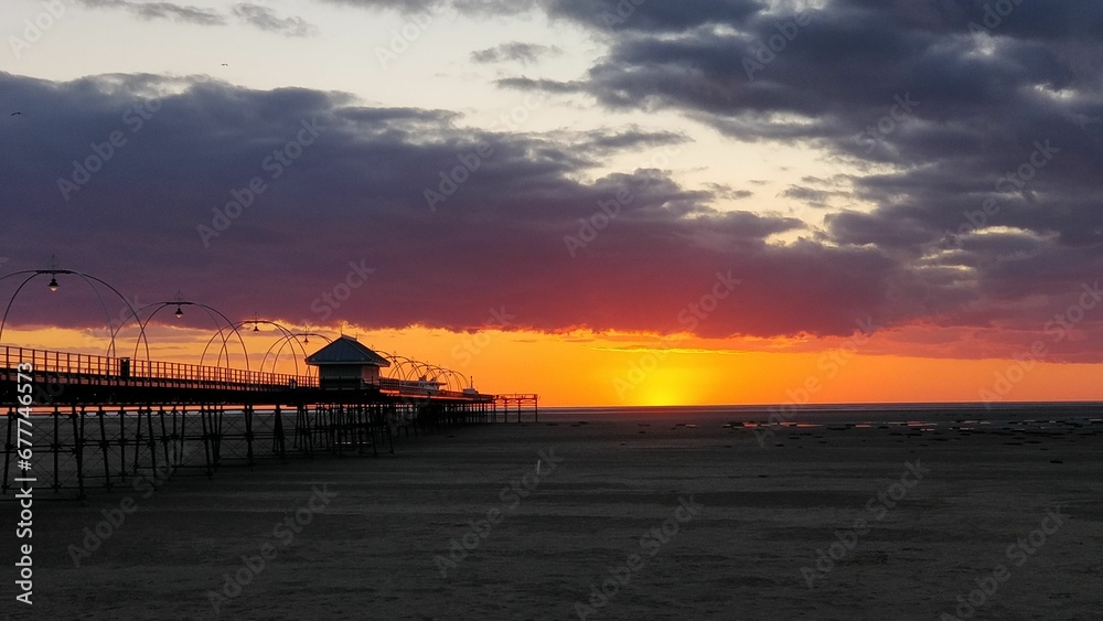 Beautiful view of a sunset at a sandy beach with a pier Beautiful view of a sunset at a sandy beach with a pier