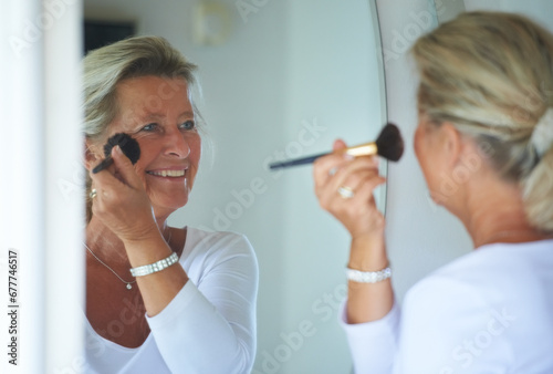 Senior woman, brush and foundation in mirror with smile, thinking and beauty to start morning in retirement. Elderly person, makeup and facial skin, reflection or happy in home bathroom for cosmetics