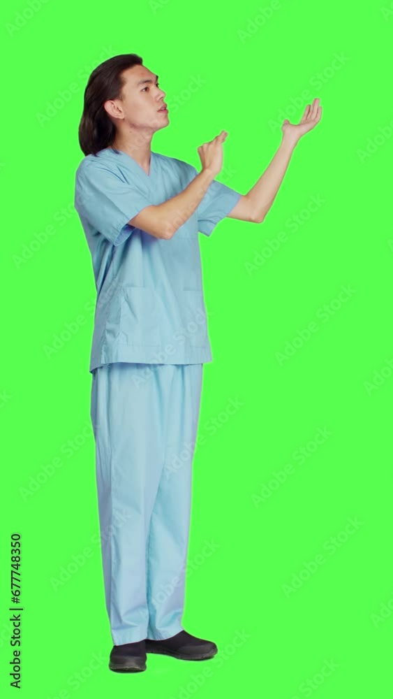 Side view working in medical industry, male specialist doing ad commercial against full body greenscreen backdrop. Medic in blue uniform points to left or right sides, presenting marketing Side view working in medical industry, male specialist doing ad commercial against full body greenscreen backdrop. Medic in blue uniform points to left or right sides, presenting marketing