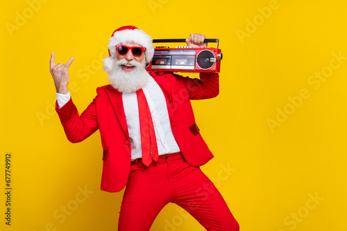 Portrait of overjoyed funky grandfather demonstrate heavy metal symbol hold boombox x-mas eve isolated on yellow color background