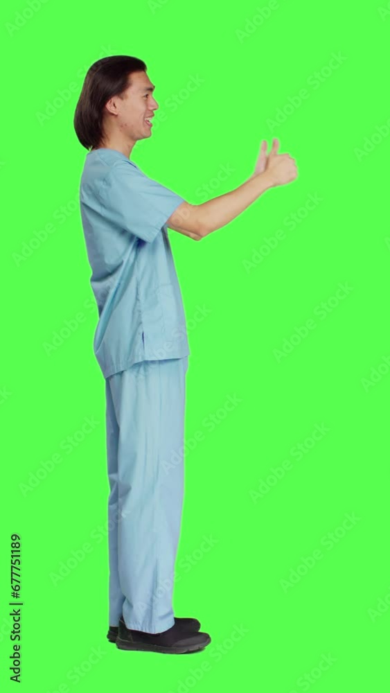 Profile of healthcare medic does thumbs up sign against isolated full body greenscreen, giving like gesture and being pleased. Medical assistant showing his agreement with okay symbol. Profile of healthcare medic does thumbs up sign against isolated full body greenscreen, giving like gesture and being pleased. Medical assistant showing his agreement with okay symbol.