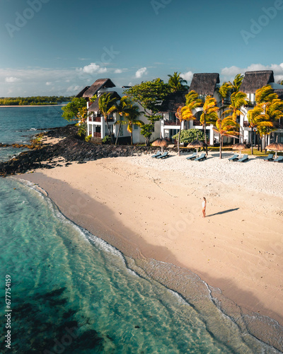 Aerial view of a woman on a luxury resort private beach along the shore with umbrellas at sunset, Ilot Lievres, Trou d'Eau Douce, Flacq district, Mauritius. photo