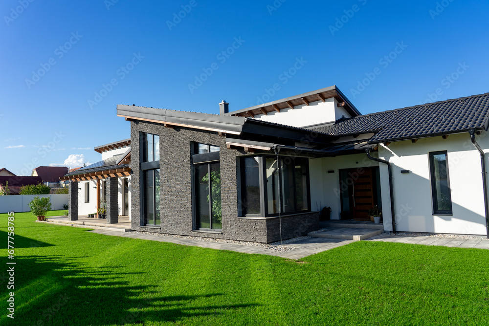 Modern house with gray stone wall and white walls in a garden witg fresh green gras