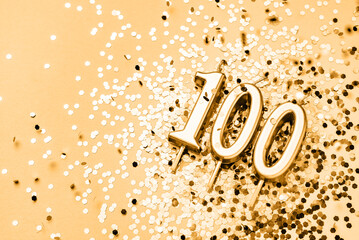 100 years celebration festive background made with golden candles in the form of number Hundred lying on sparkles. Universal holiday banner with copy space.