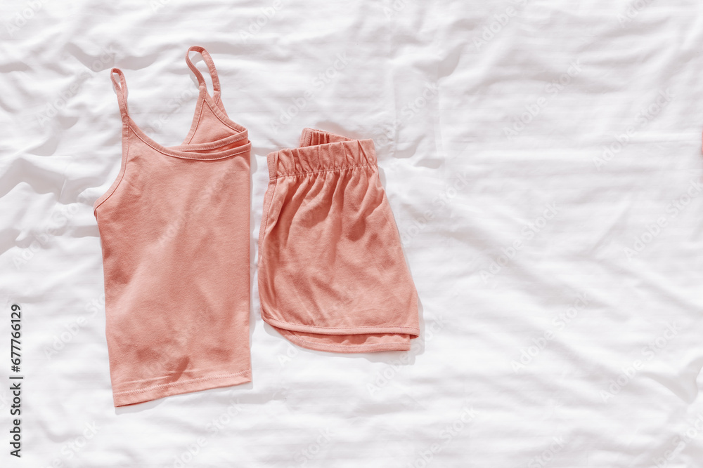 Top view pink pajama folded on white crumpled bedclothes. Cozy pyjama for comfort rest at night. Flat lay of singlet and shorts, sleeping suit pastel pink color, sleepwell concept, empty space Top view pink pajama folded on white crumpled bedclothes. Cozy pyjama for comfort rest at night. Flat lay of singlet and shorts, sleeping suit pastel pink color, sleepwell concept, empty space