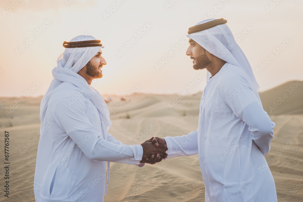 Obraz premium Two business men wearing traditional uae white kandura spending time in the desert of Dubai