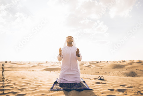 Photography Man with white traditional kandura from uae praying in the desert on the carpet