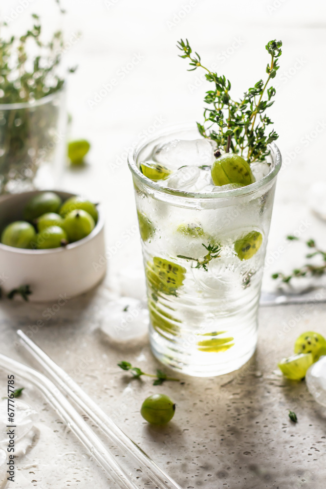 Glass of refreshing iced detox drink with gooseberries and thyme. Infused water or berry cocktail