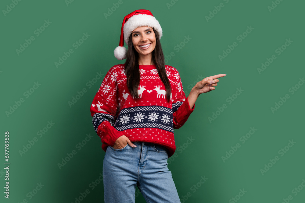Photo of cute adorable lady santa helper dressed print xmas sweater pointing finger empty space isolated green color background Photo of cute adorable lady santa helper dressed print xmas sweater pointing finger empty space isolated green color background