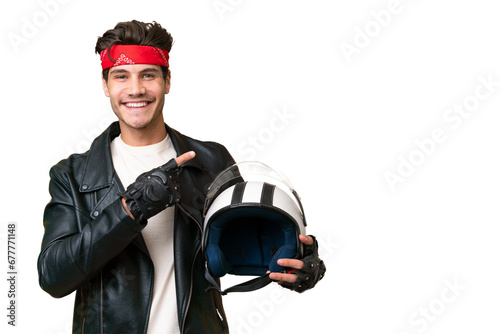 Young caucasian man with a motorcycle helmet over isolated background pointing to the side to present a product