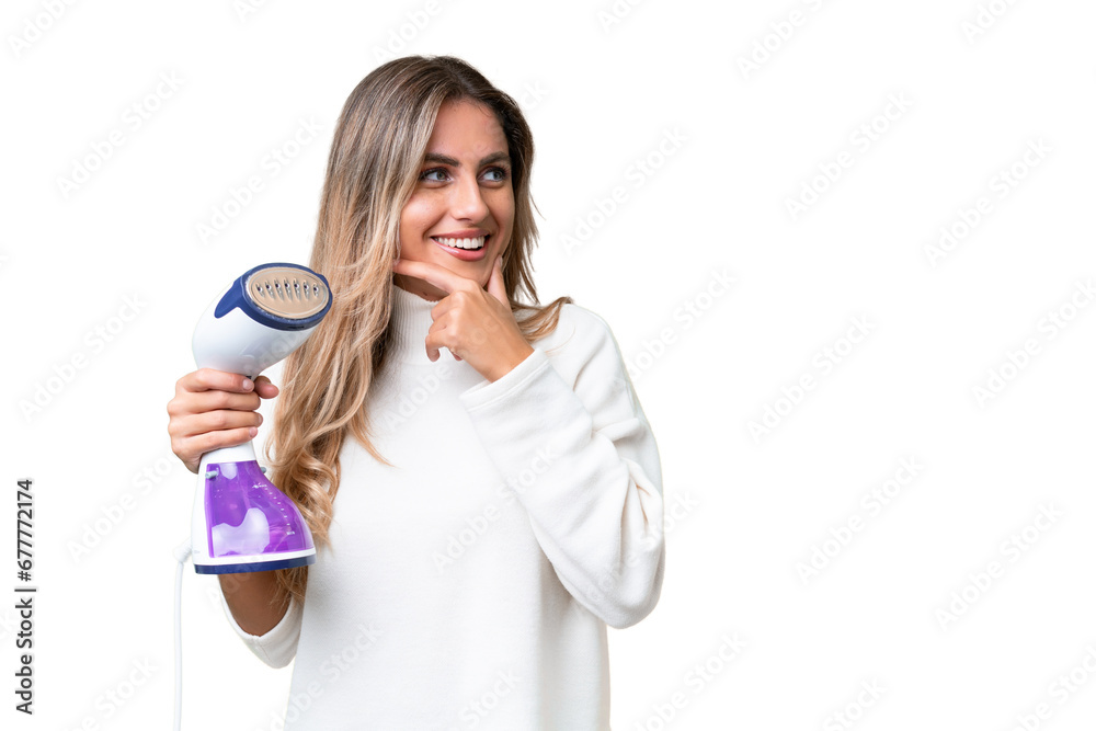 Young Uruguayan woman holding an iron over isolated background thinking an idea and looking side Young Uruguayan woman holding an iron over isolated background thinking an idea and looking side