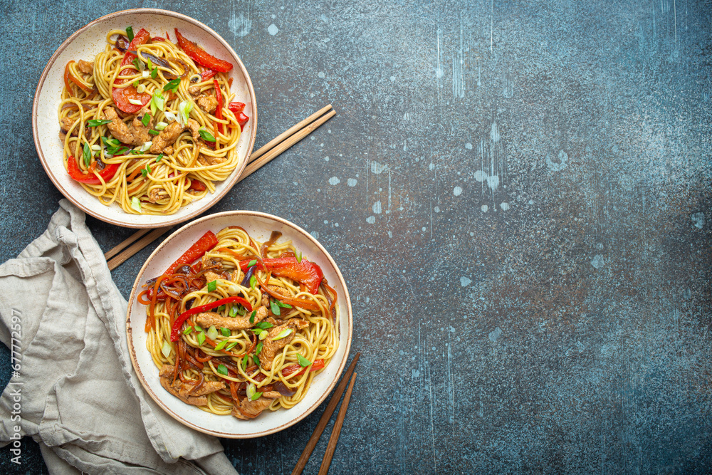 Φωτογραφία Two bowls with Chow Mein or Lo Mein, traditional Chinese stir fry noodles with meat and vegetables, served with chopsticks top view on rustic blue concrete background, space for text