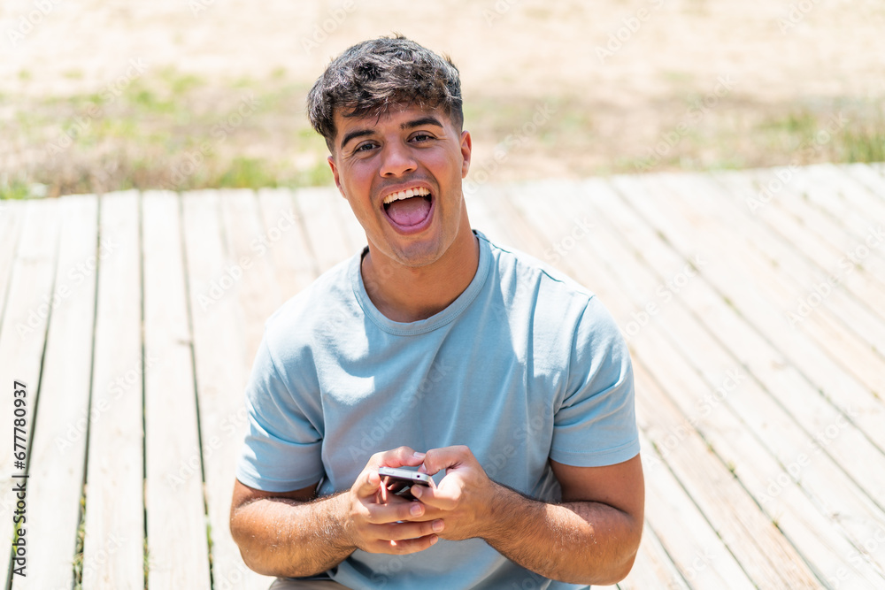 Fototapeta premium Young hispanic man at outdoors surprised and sending a message