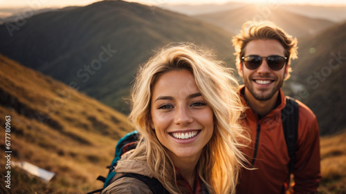 A cheerful couple of hikers taking selfies on the top of the mountain, millennial boy and girl enjoying the day laughing together looking at camera. Travelers, space for text