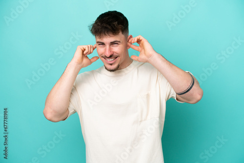 Young caucasian handsome man isolated on blue background frustrated and covering ears