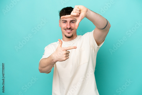 Young caucasian handsome man isolated on blue background focusing face. Framing symbol