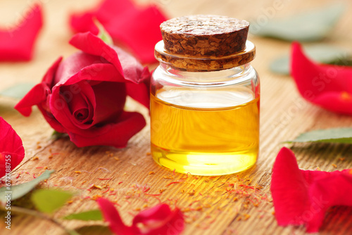 Fototapeta Naklejka Na Ścianę i Meble -  Rose essential oil or water in glass bottle with red flowers and petals on textured table, closeup, copy space, massage and spa, cosmetics ingredient, natural healthy hair and face skin care concept
