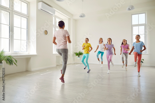 Smiling girls training dance moves in studio with female choreographer. Group of happy kids doing dance workout in choreography class. Children sport and healthy lifestyle concept.