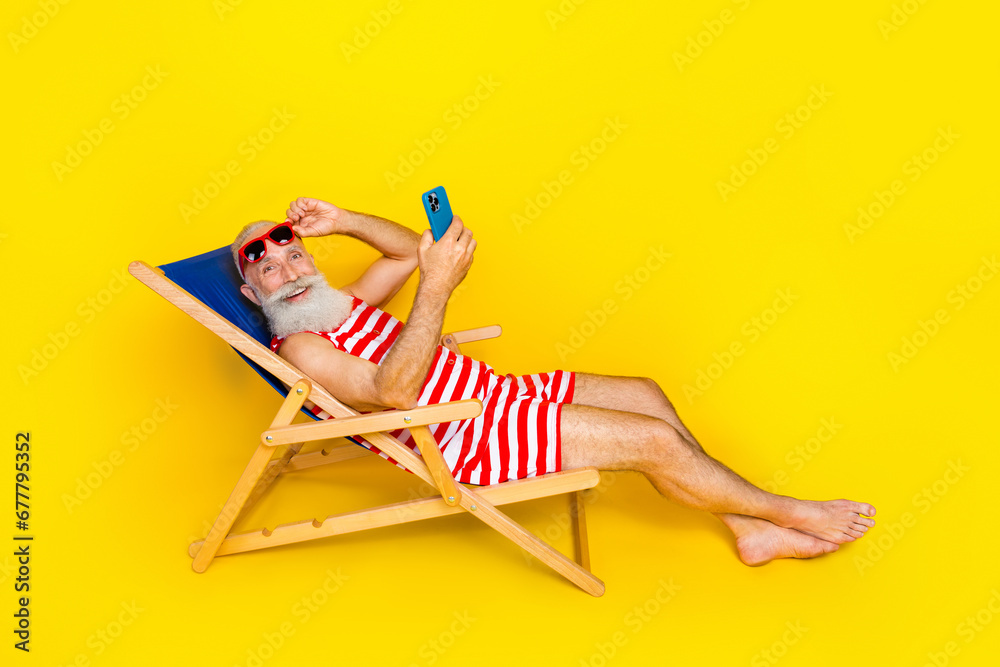 Full length photo of carefree old man lying on sunbed at turkish resort using smartphone and relaxing isolated on yellow color background Full length photo of carefree old man lying on sunbed at turkish resort using smartphone and relaxing isolated on yellow color background