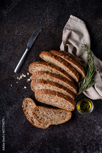 Sliced sourdough bread from whole grain flour and pumpkin seeds on a grid, olive oil and black olive on a rustic wooden table. Artisan bread.
