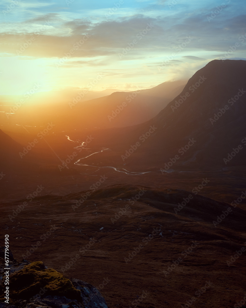 A winding road between mountain ranges illuminated by the rising sun. A82 road opposite Buachaille Etive Mor at dawn. Scotland