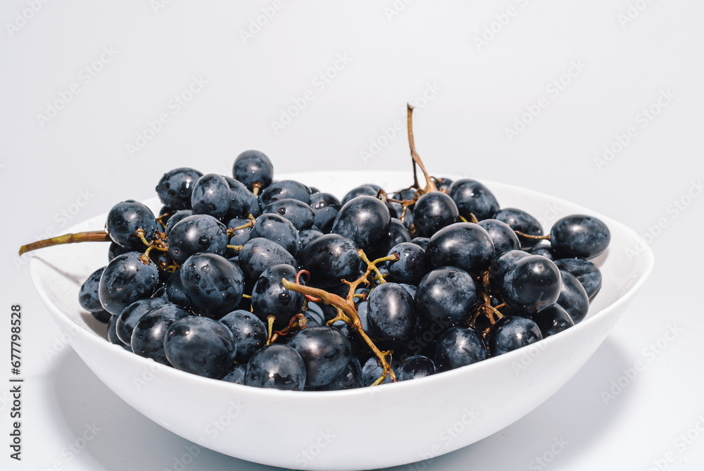 Bunches of blue grapes in a white plate on a white background. Berries, summer harvest, healthy eating Bunches of blue grapes in a white plate on a white background. Berries, summer harvest, healthy eating