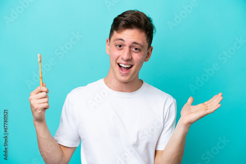 Young Brazilian man brushing teeth isolated on blue background with shocked facial expression