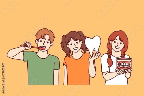 Small children with toothbrush and model teeth are urged to follow rules of oral hygiene and visit dentist on time. Three happy kids with smile demonstrate desire to have healthy and beautiful teeth