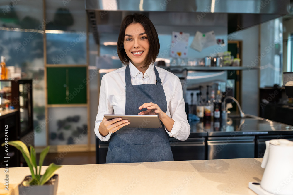Cute dark-haired coffee shop assistant with a tablet in hand smiling nicely Cute dark-haired coffee shop assistant with a tablet in hand smiling nicely