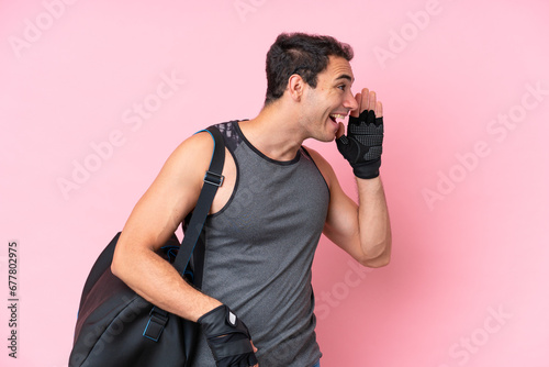 Young sport caucasian man with sport bag isolated on pink background shouting with mouth wide open to the lateral photo