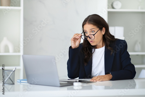 Shocked businesswoman sitting at office, looking at laptop screen