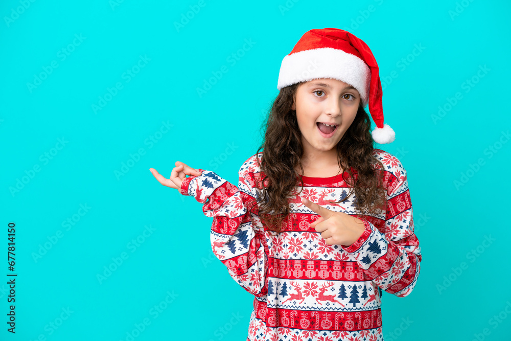 Little caucasian with christmas hat isolated on blue background surprised and pointing side Little caucasian with christmas hat isolated on blue background surprised and pointing side