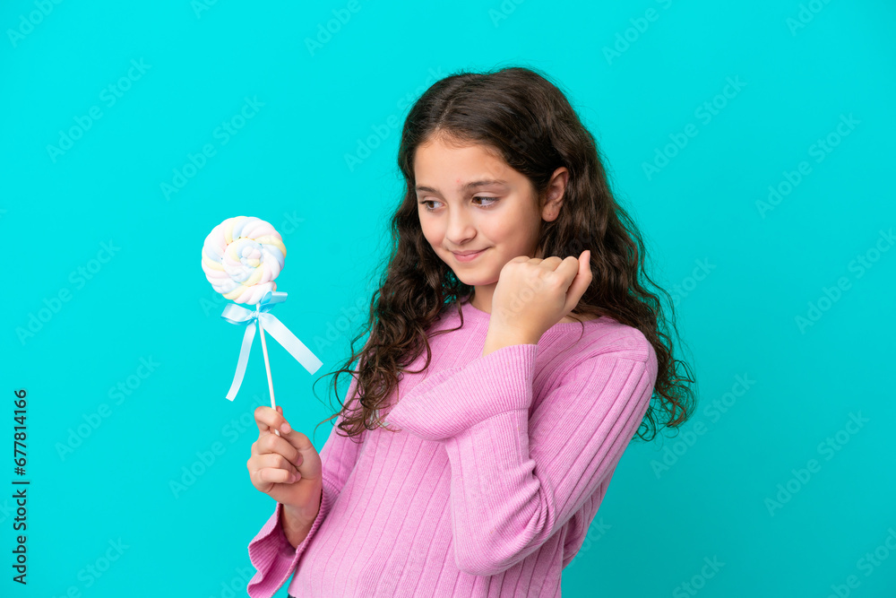 Little caucasian girl holding a lollipop isolated on blue background celebrating a victory Little caucasian girl holding a lollipop isolated on blue background celebrating a victory