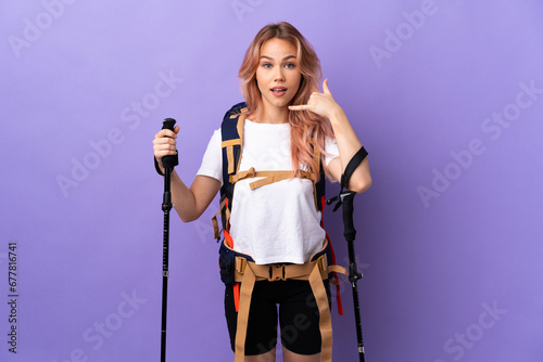 Teenager girl with backpack and trekking poles over isolated purple background making phone gesture. Call me back sign