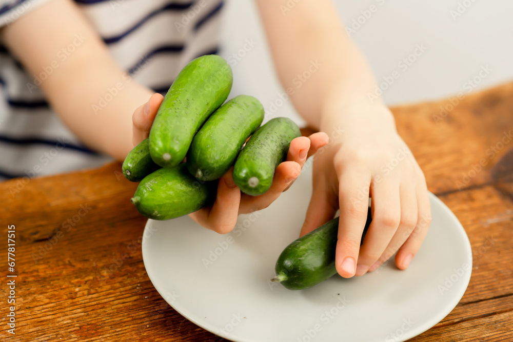 Farm-to-table freshness: Child's hands presenting crisp green cucumbers on a wooden surface Farm-to-table freshness: Child's hands presenting crisp green cucumbers on a wooden surface