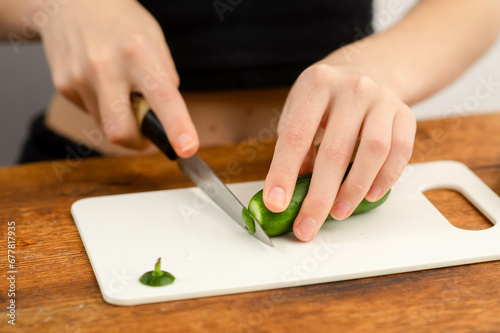 Culinary greenery: Female hands skillfully cut fresh cucumbers, highlighting the culinary artistry of crafting a salad and the health benefits of green vegetables